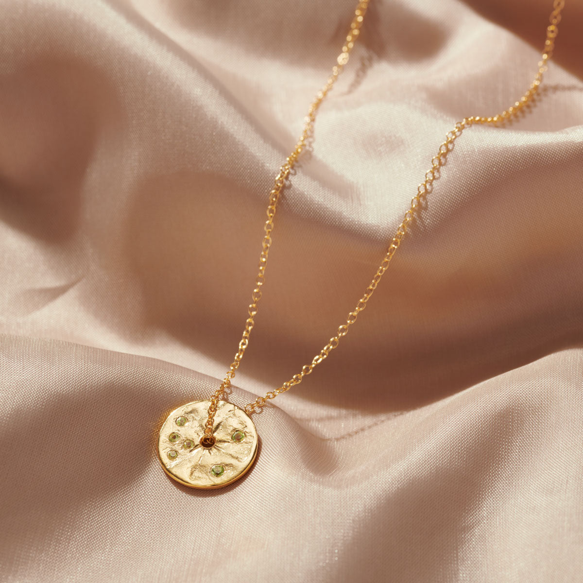 Pretty gold spinning disc pendant on gold chain set with six green peridot gemstones, making it the ideal gift for an August birthday.tones