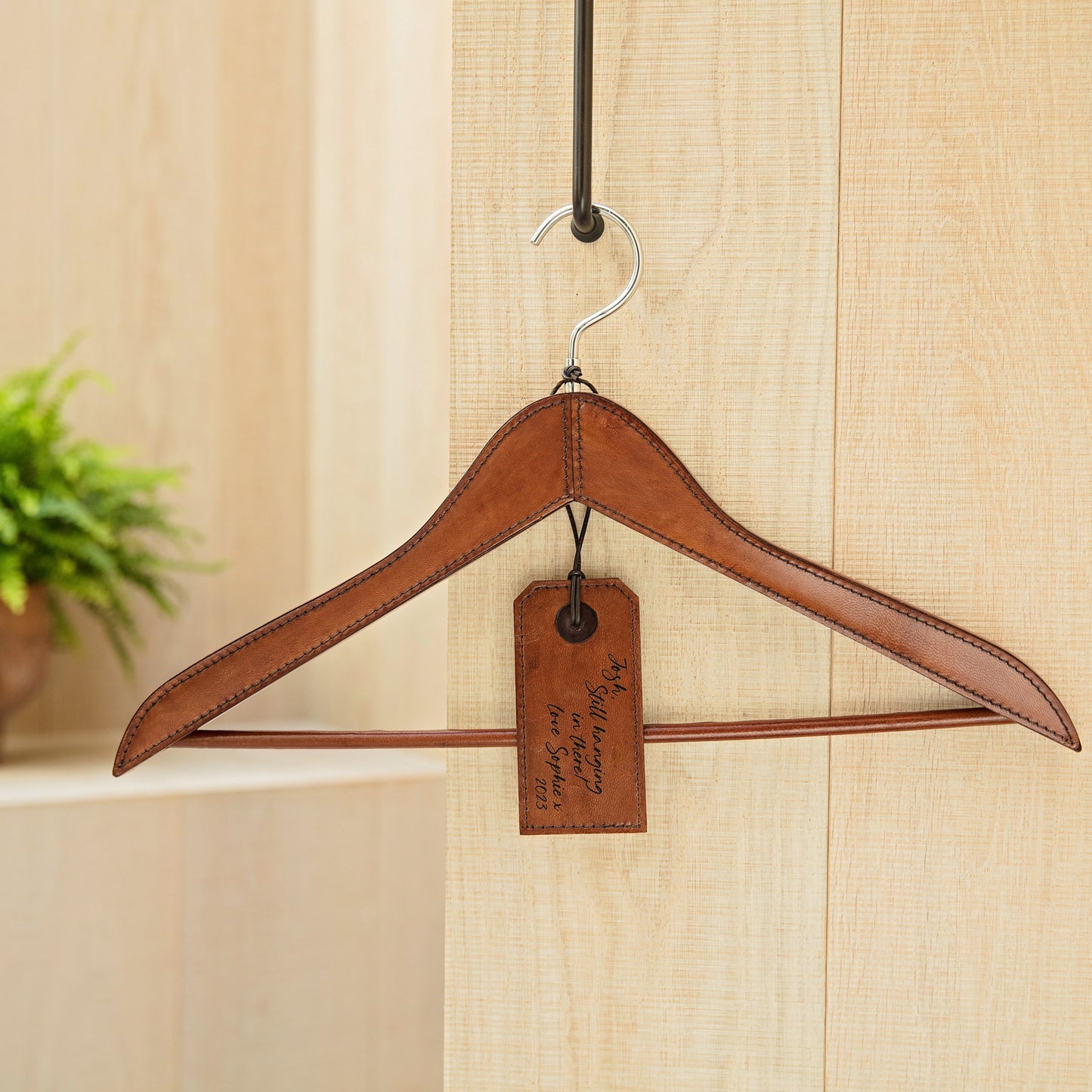 Personalised tan leather coat hanger for hanging suits, dresses or coats. Smooth handstitched finish protects clothes. Give as a thoughtful best man gift or unique new home present.