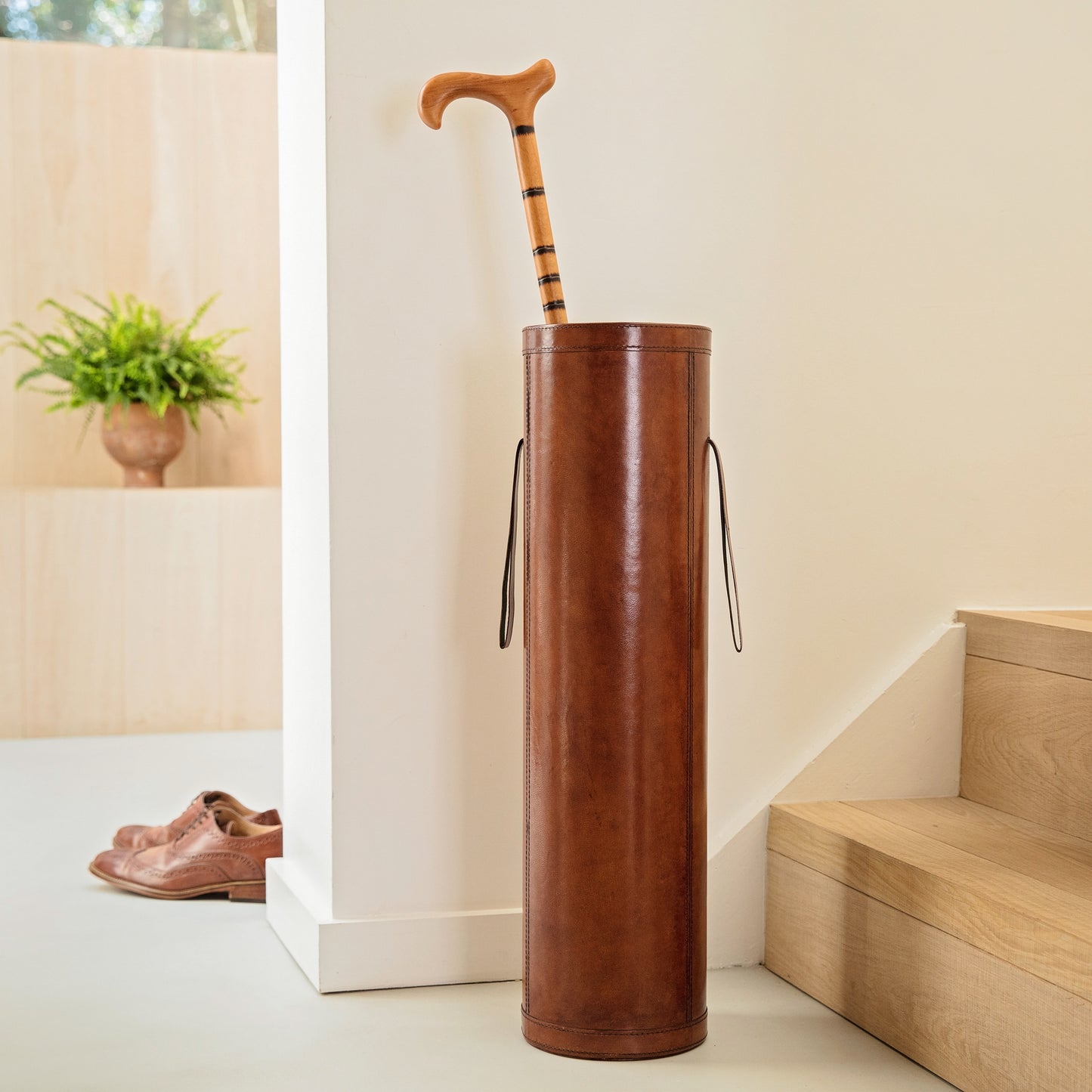 tan leather stick stand in tan with wooden walking stick in hallway