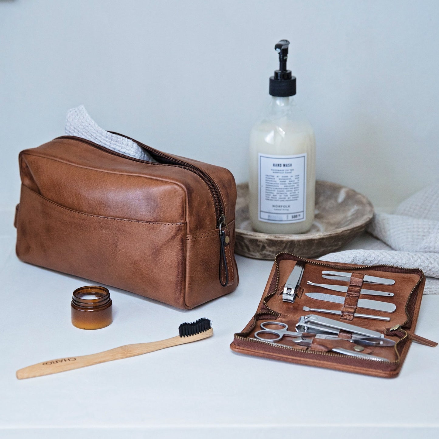 Men’s grooming kit combining a personalised wash bag and men’s manicure set in soft, supple tan leather. Add initials or a name as a thoughtful leather anniversary gift for him or personalised Father’s Day gift.