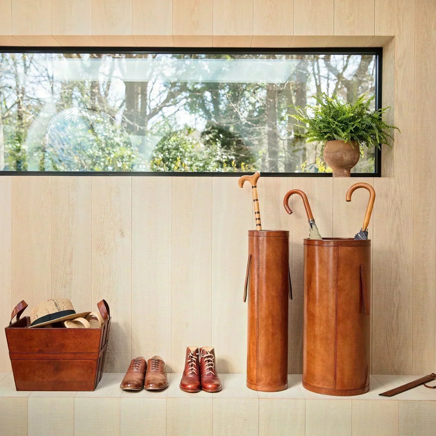 Wooden hallway featuring leather umbrella stand and leather basket for show storage. 