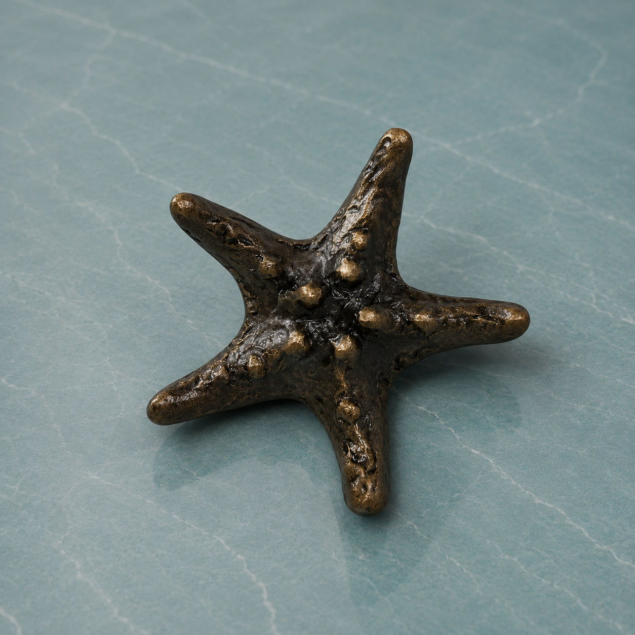 A miniature bronze starfish figurine with a textured, metallic finish, displayed on a light blue-gray stone surface.