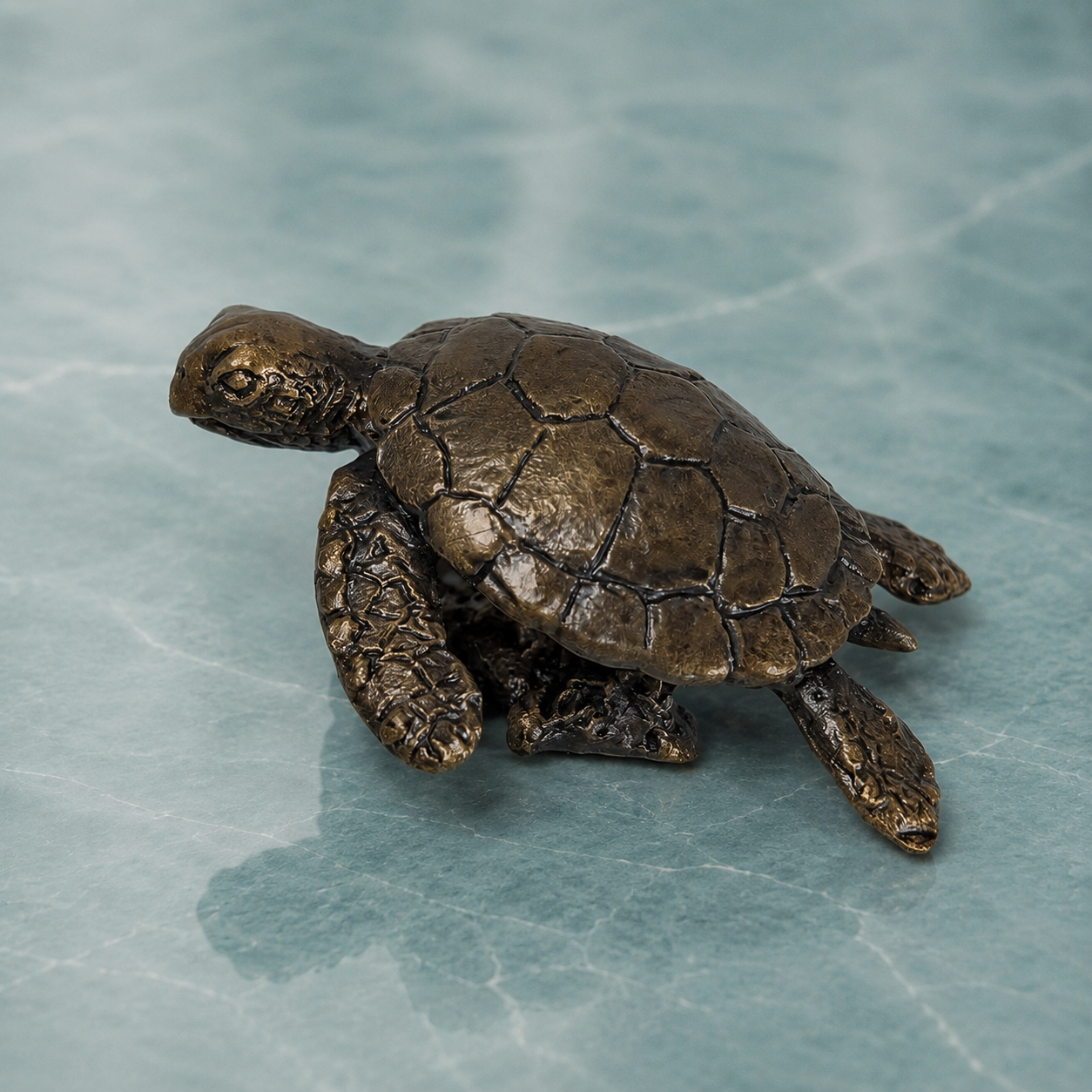 A small bronze sea turtle figurine with a textured, metallic finish, resting on a light blue marble-patterned surface.