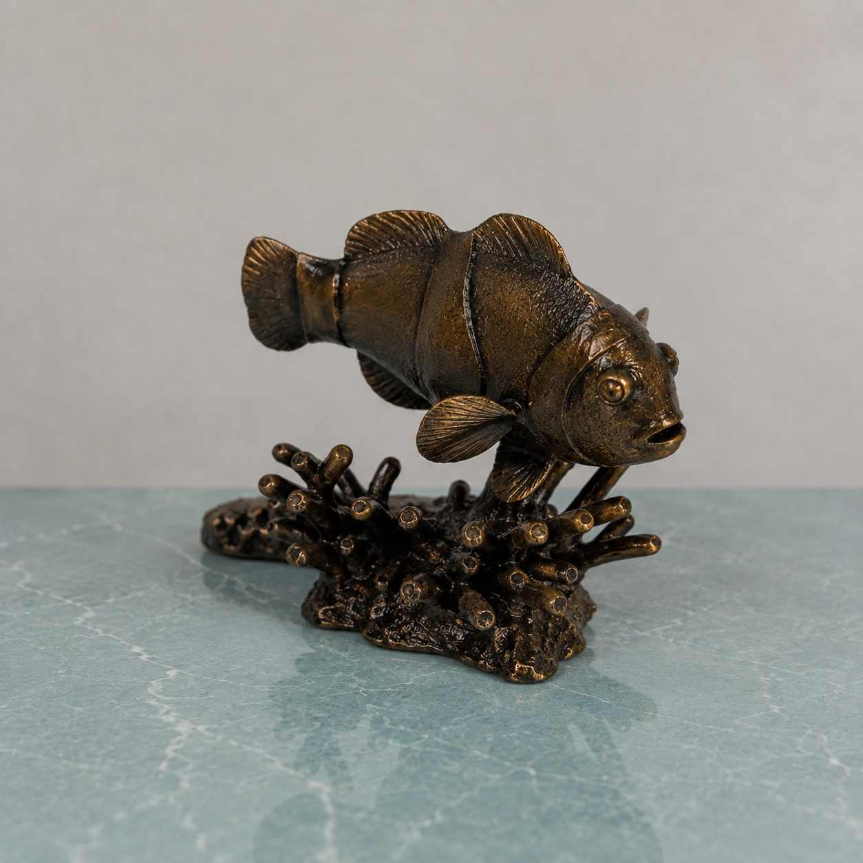 Bronze clownfish sculpture perched on a coral base, displayed on a pale blue marble surface .